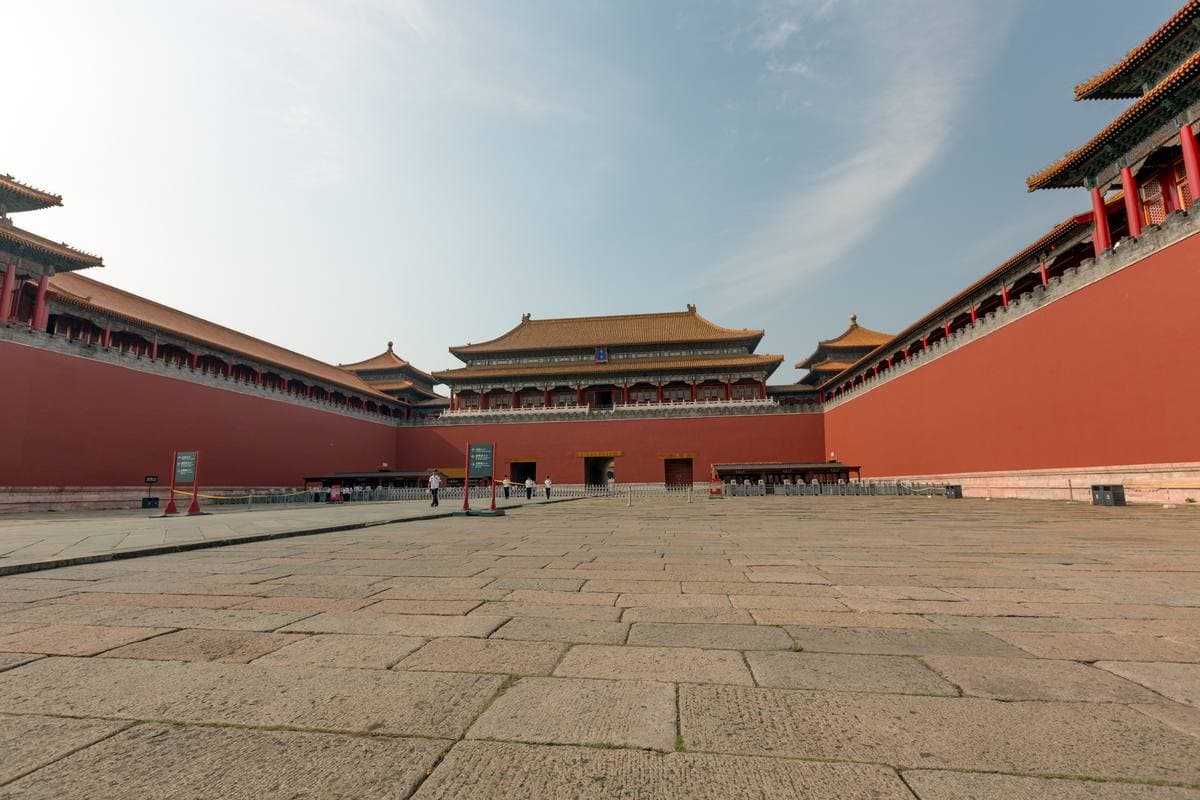 A vast red gatehouse with yellow-tiled roofs across a stone square