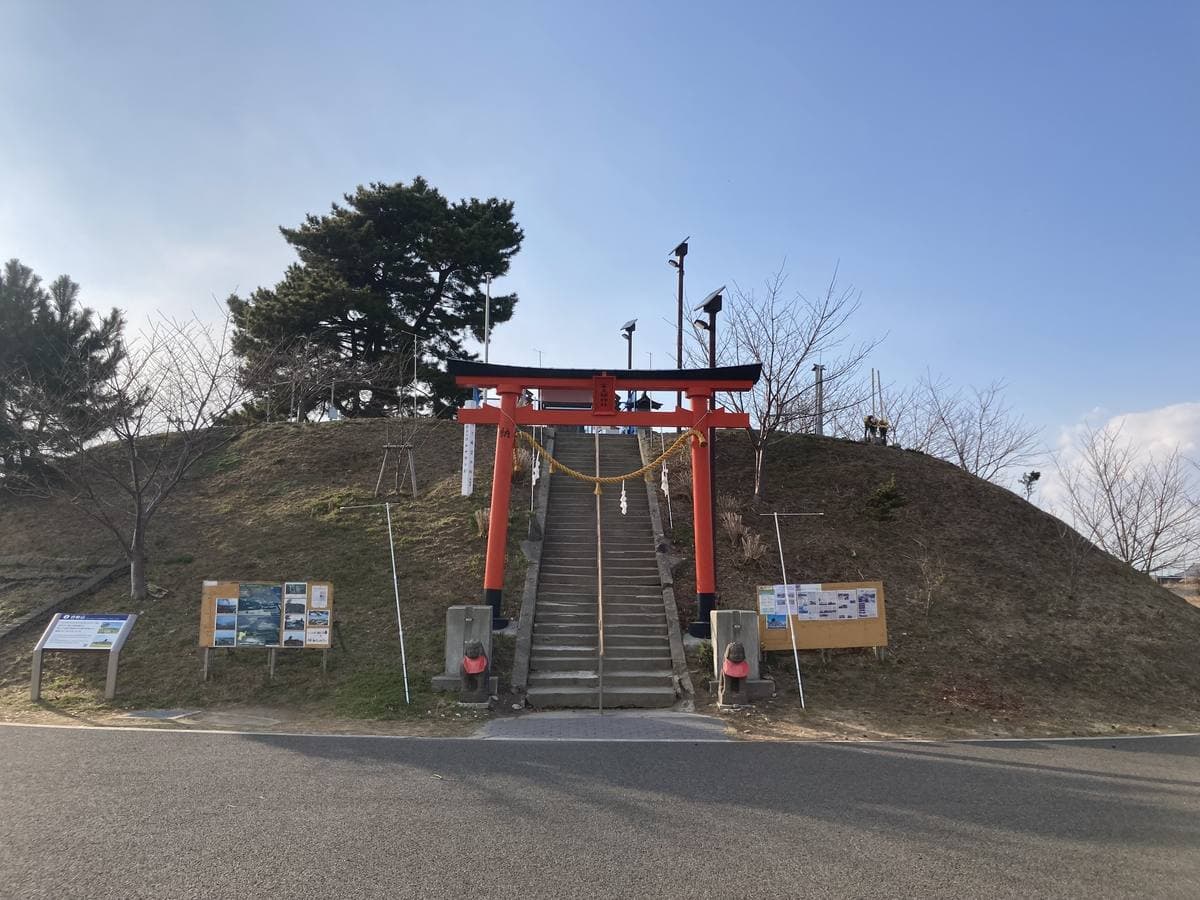 A small grassy mound with a red torii gate and steps up it under a pale sky