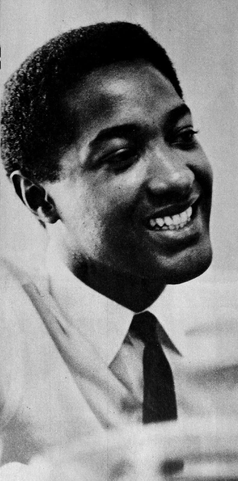 Sam Cooke smiling broadly, head turned to one side, in a white shirt and dark tie