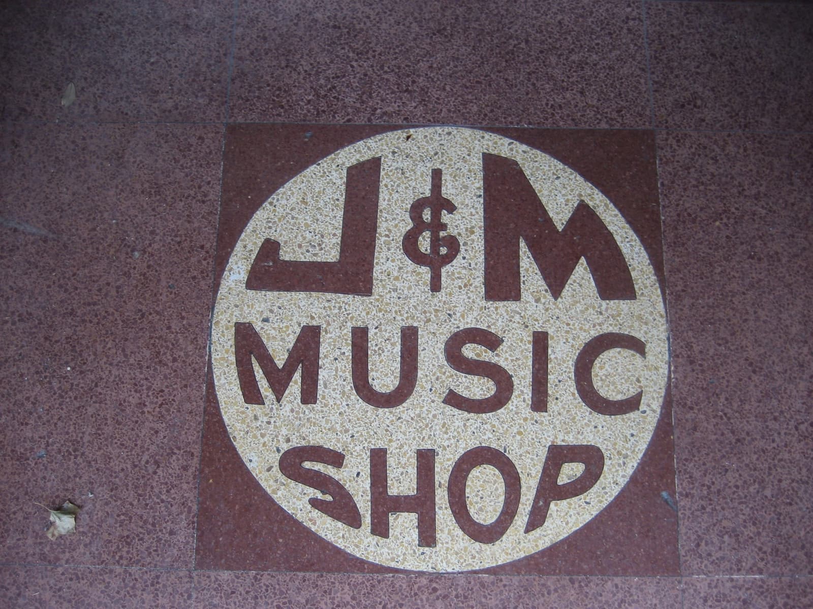 A round terrazzo floor sign reading J&M Music Shop at a doorway