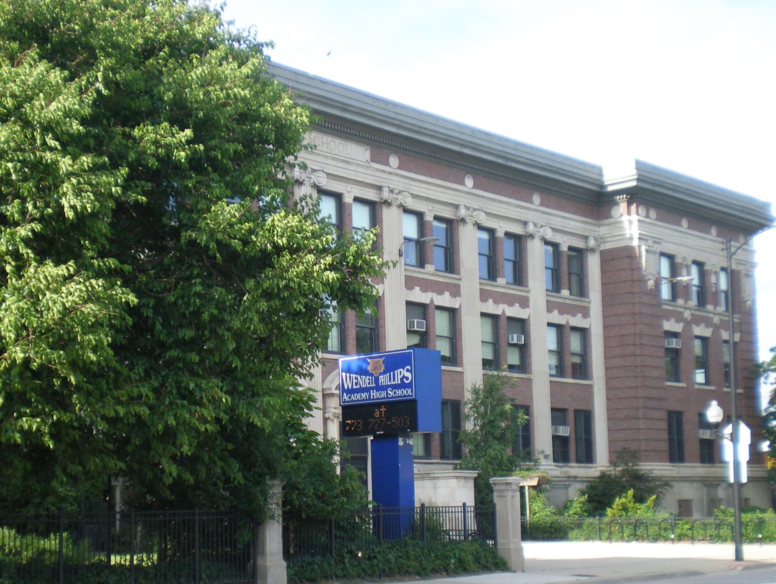 A four-storey red-brick school building behind trees and an iron fence on a Chicago street