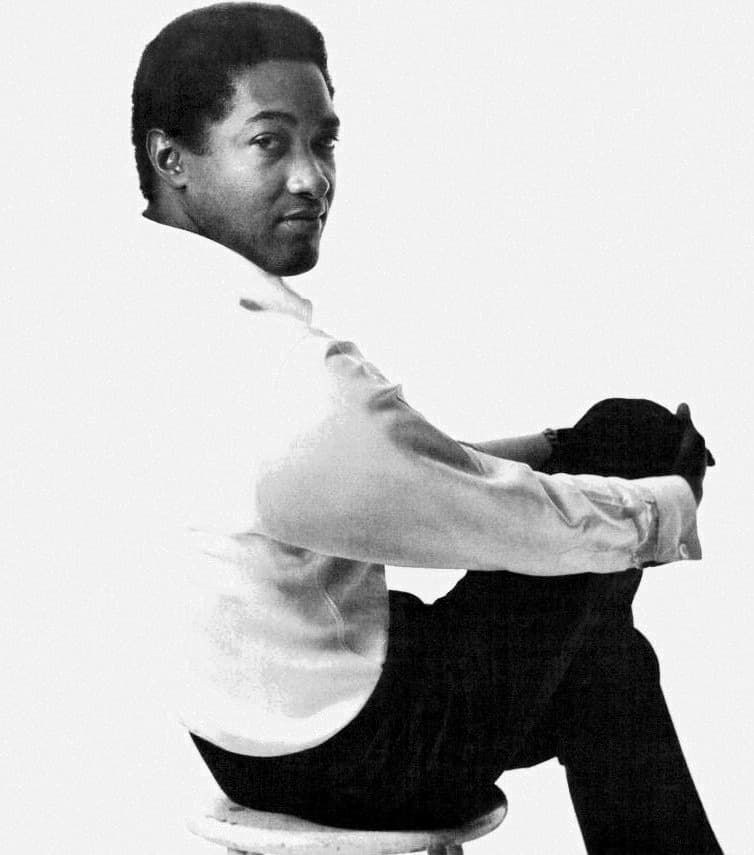 Sam Cooke in a white shirt and dark trousers, sitting sideways on a stool and looking back over his shoulder