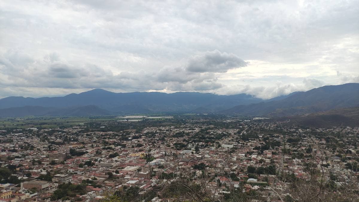 A small Mexican town of low roofs and a church spread across a green valley