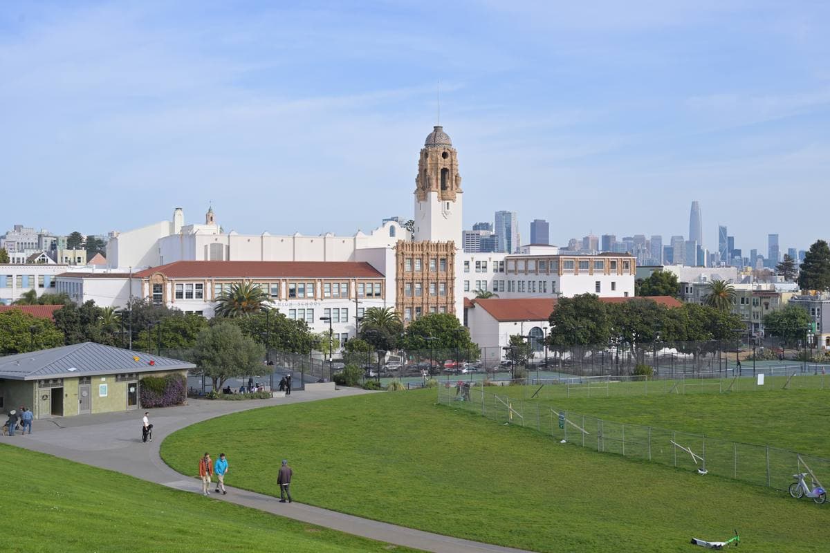 A white Spanish-style school building with a tall domed tower above a park