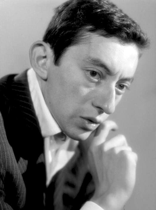 Serge Gainsbourg in black and white, dark jacket and open white collar, chin resting on his hand