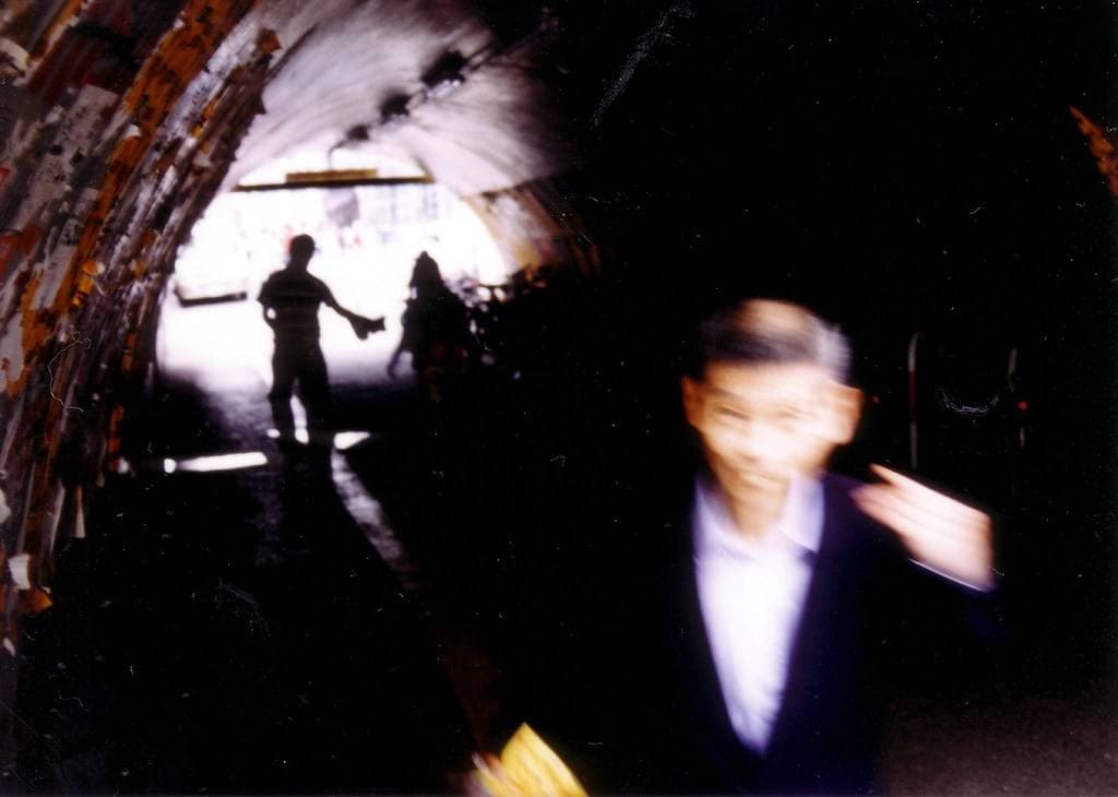 A man in a suit hurrying through a dark arched tunnel, figures silhouetted against the light at the far end