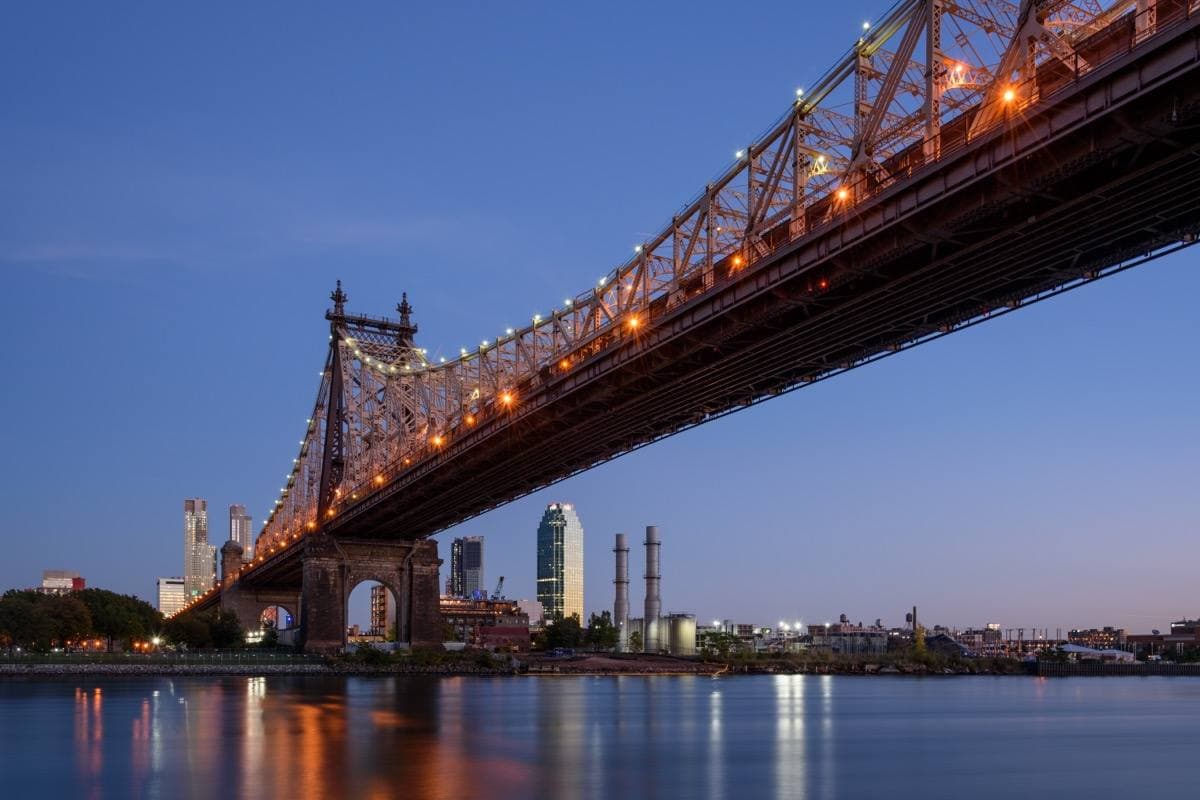 A steel cantilever bridge lit up at dusk over a dark river