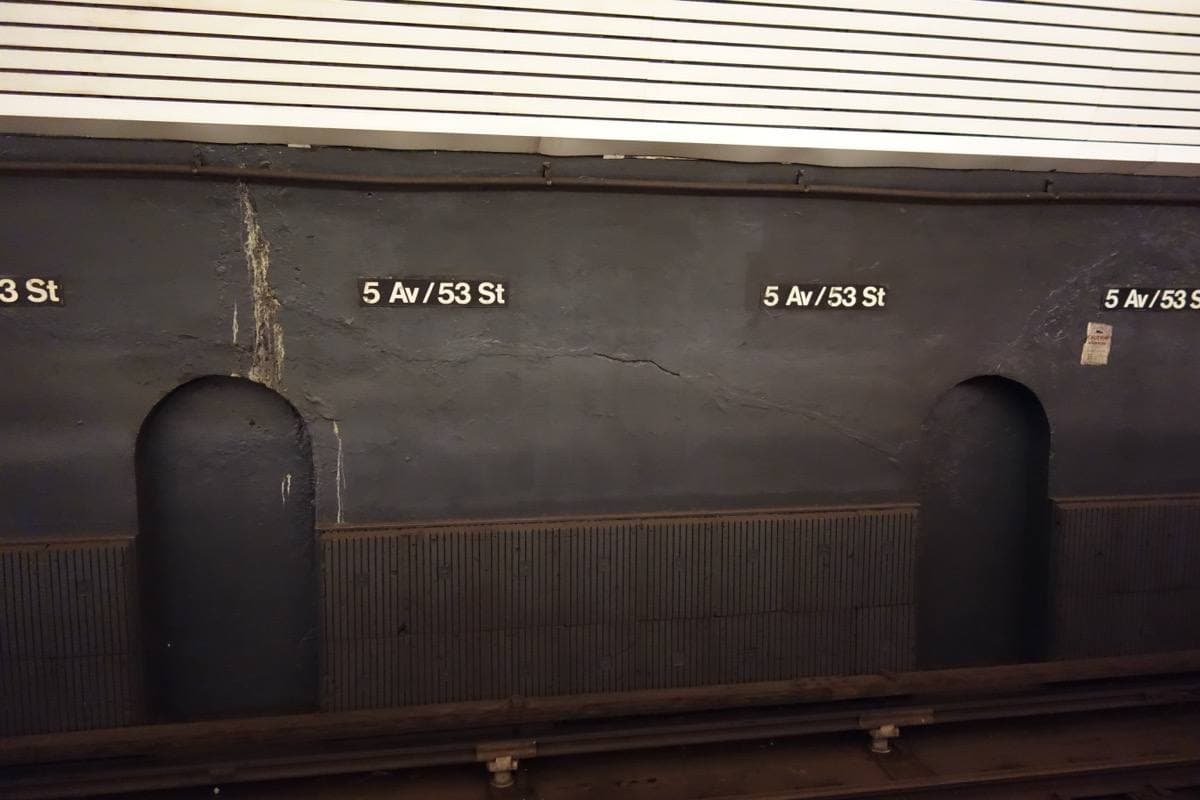 A grey tunnel wall with arched recesses and 5 Av / 53 St name tiles