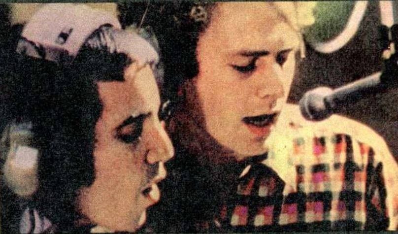 Paul Simon in headphones and Art Garfunkel singing at a microphone, close up
