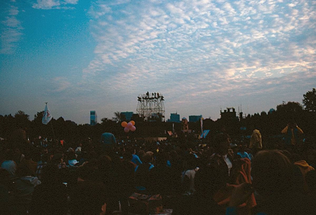 A huge crowd on a lawn facing a distant lit stage