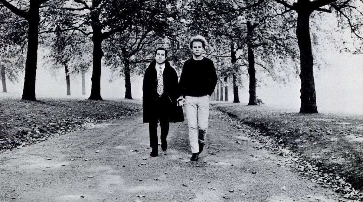 Two small figures in dark coats walking down a long avenue of bare trees