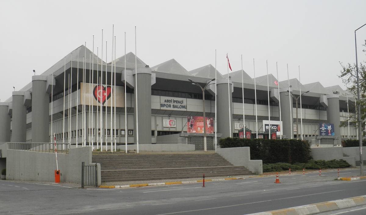 A grey concrete sports hall with flagpoles along its front