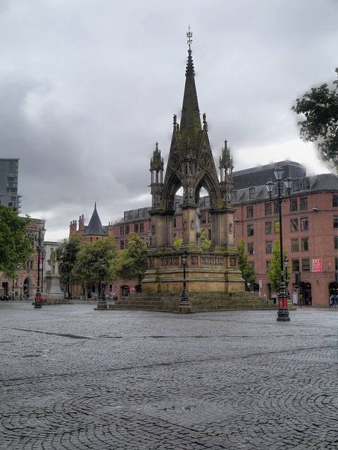 A grey stone square with a Gothic memorial and red-brick buildings