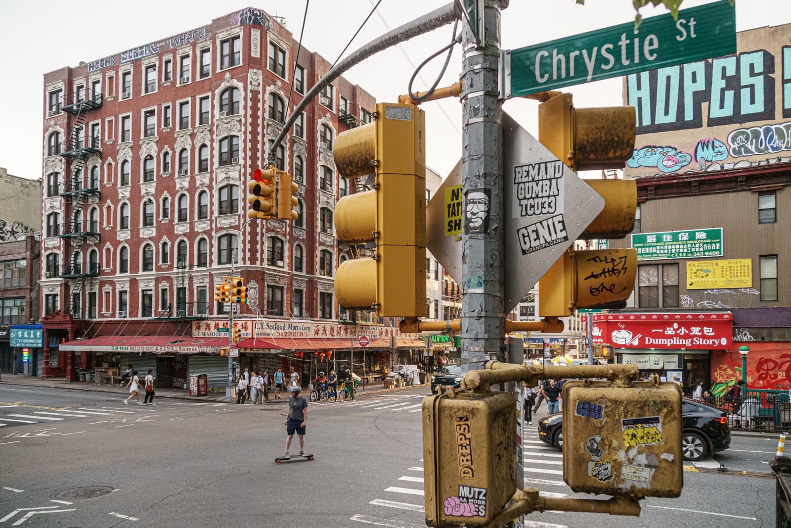 A busy street corner with a green street sign reading Chrystie St and a red brick block