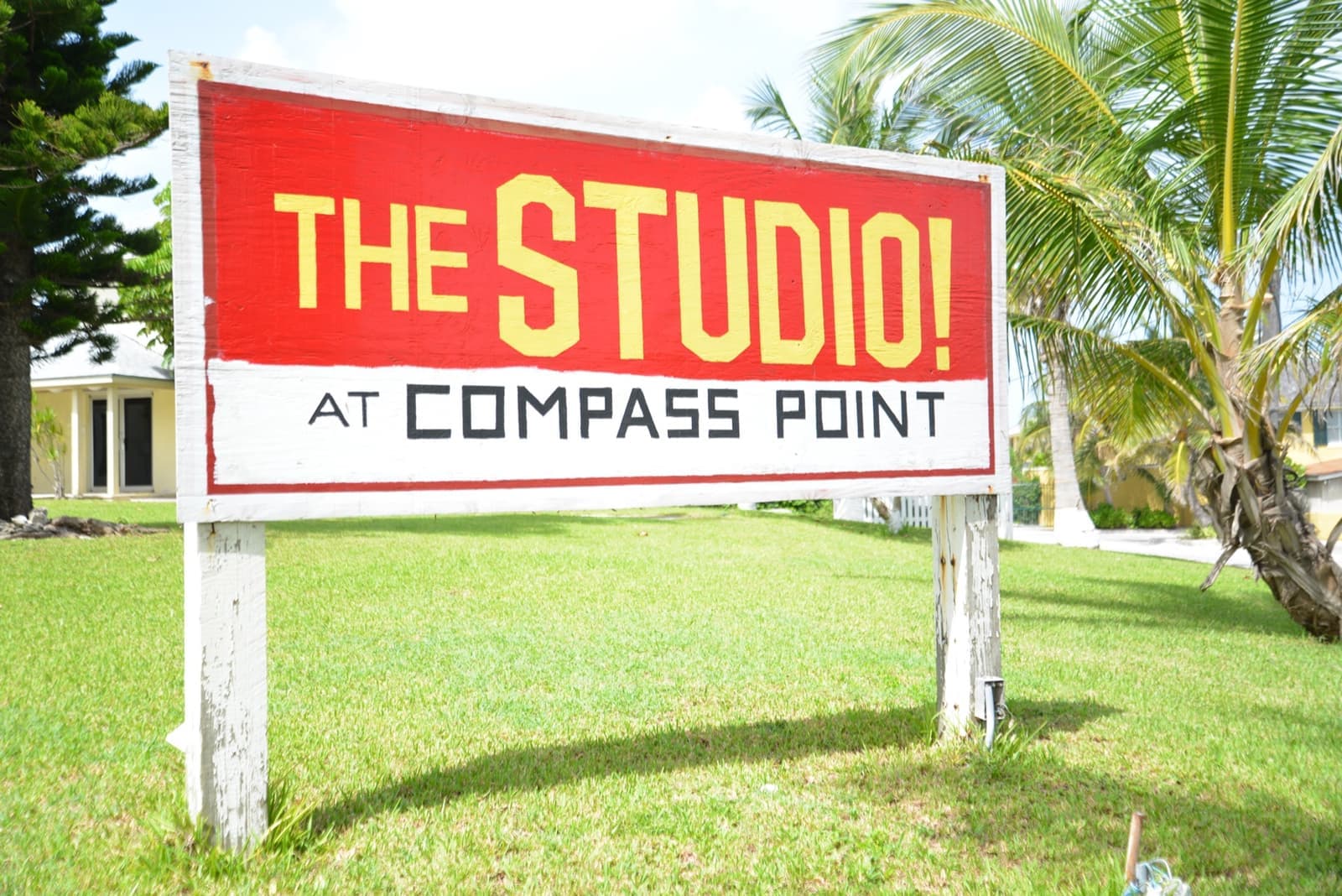 A bright red sign on a lawn reading The Studio at Compass Point, with palm trees behind