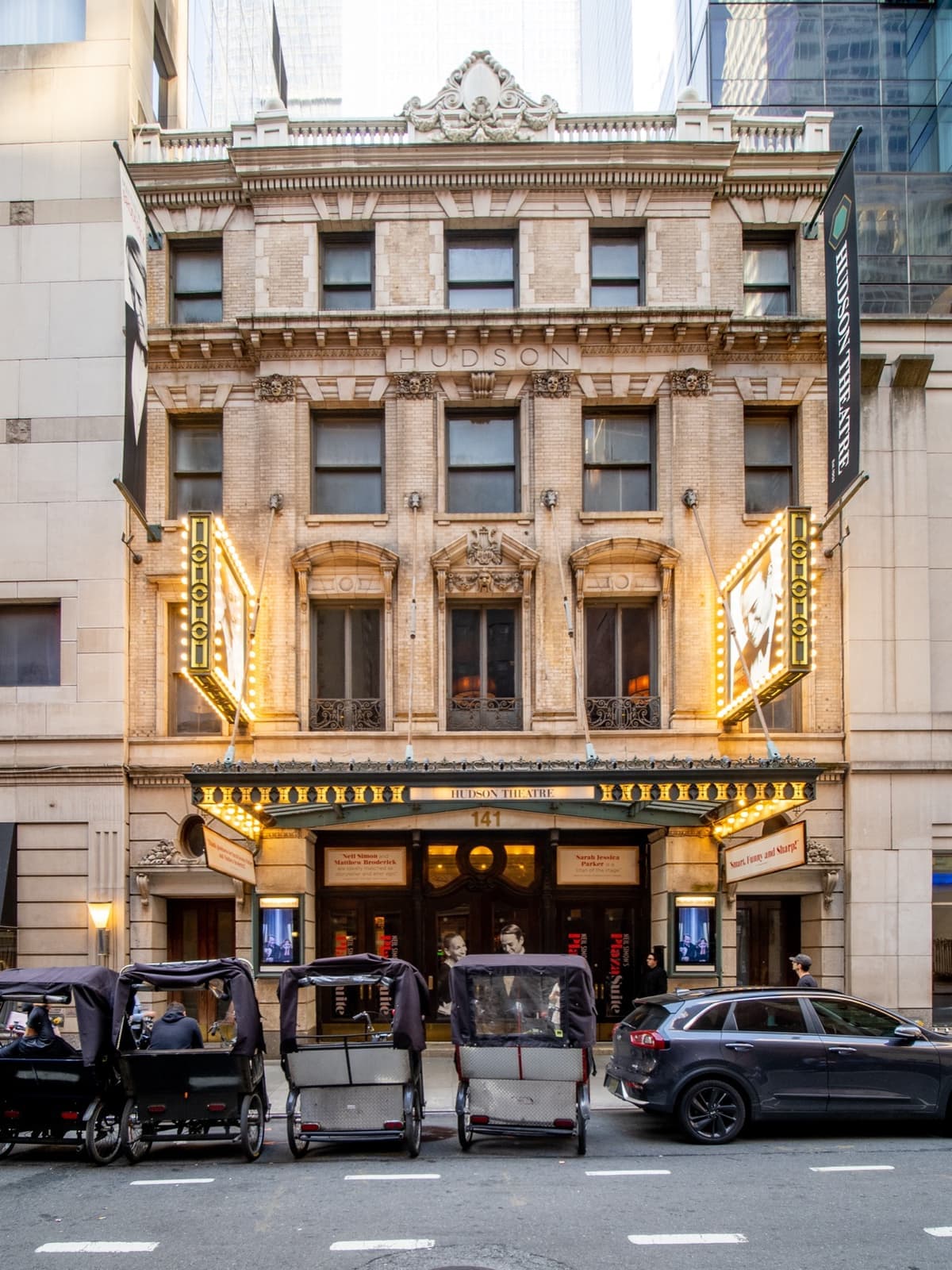 An ornate stone theatre front in Midtown with lit lamps over the doors