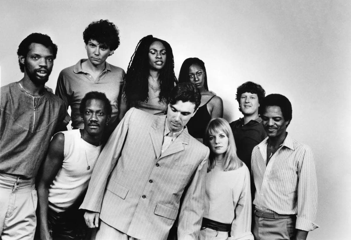 Nine musicians in a black-and-white group photo, David Byrne in an oversized pale suit at the centre