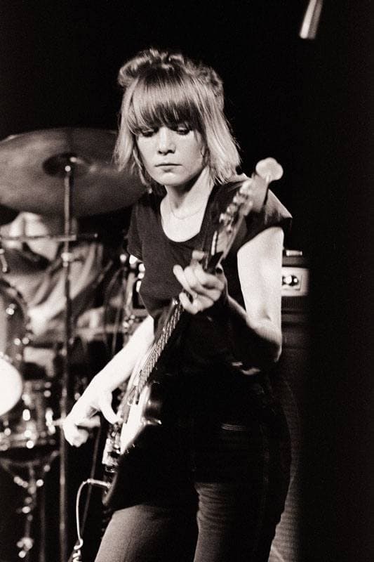 Tina Weymouth playing bass in front of a drum kit, black and white