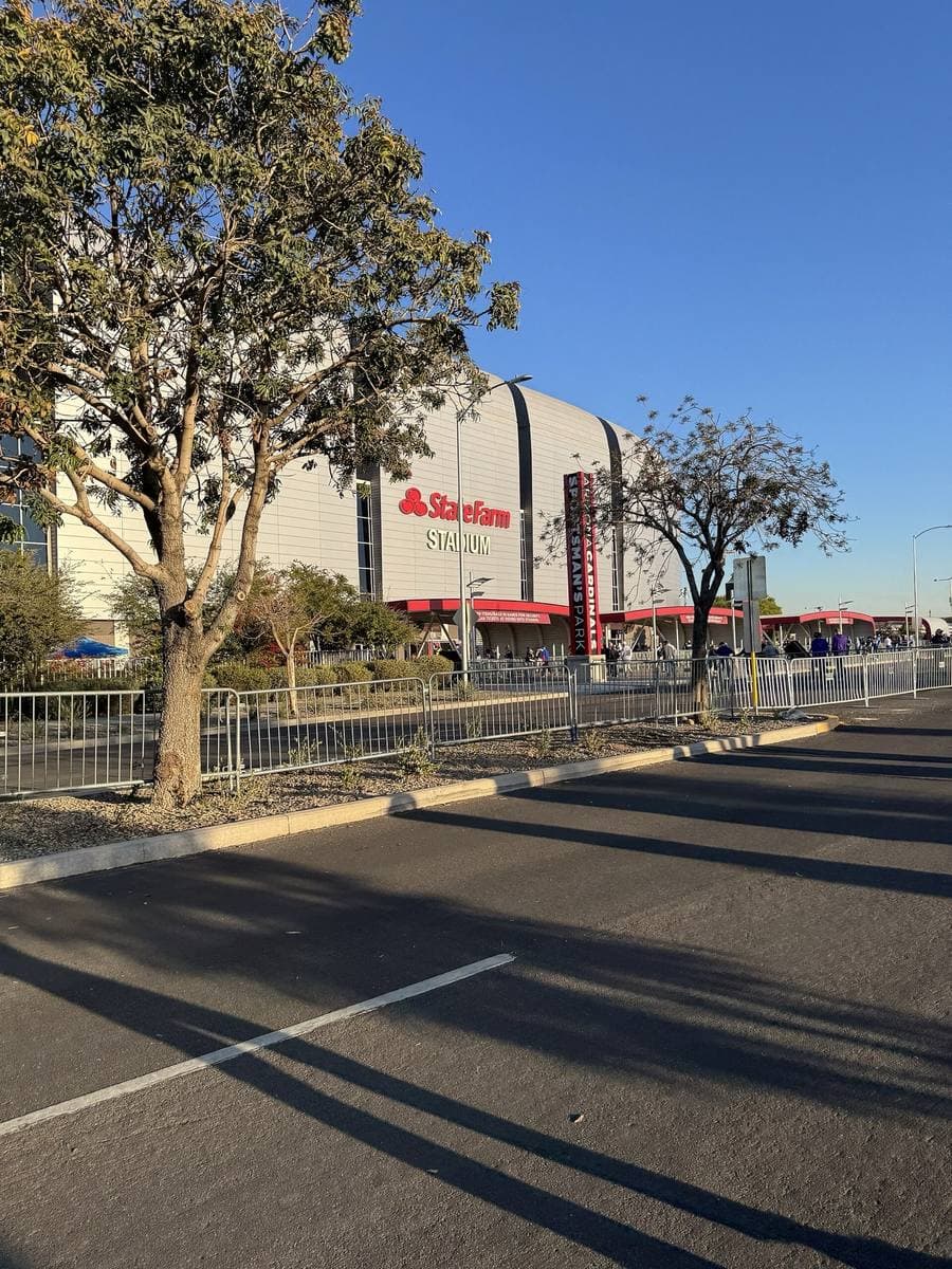 A silver stadium beyond a wide empty road and a row of trees