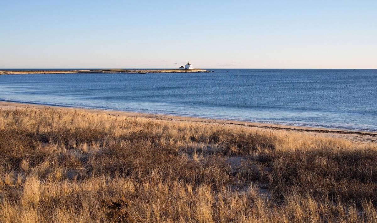A white lighthouse on a rocky point across calm grey water