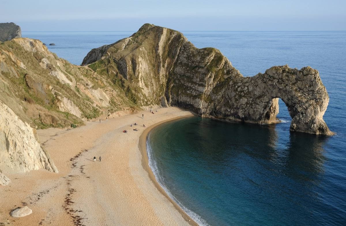 The limestone arch of Durdle Door standing in a blue sea below chalk cliffs