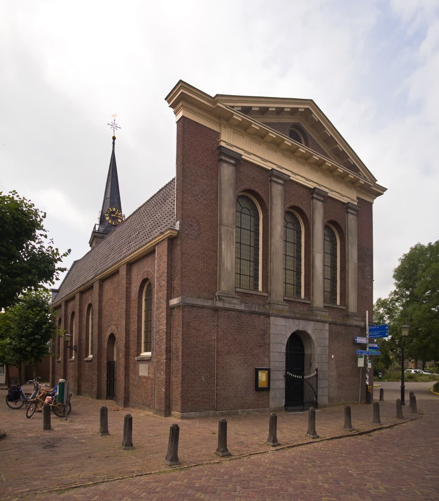 A brick church with a tall pediment and slim spire on a cobbled square