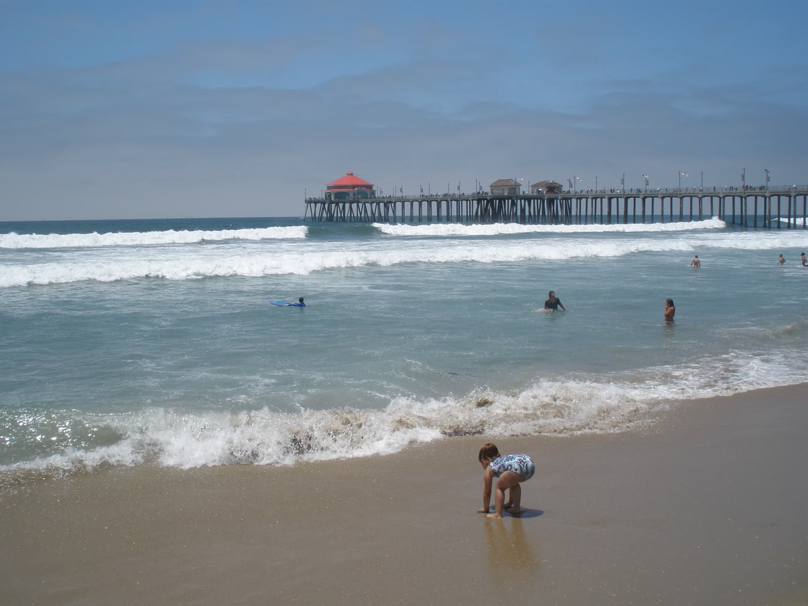 Waves breaking on a wide beach with a long pier running out to sea and a child playing in the shallows