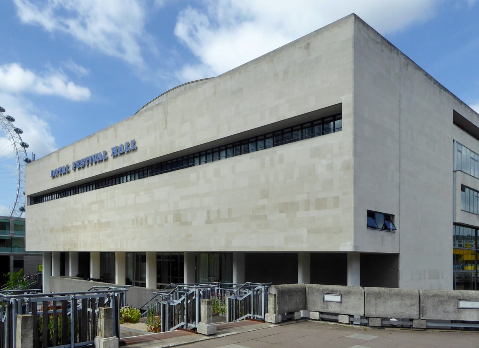 A long pale modernist concert hall under a blue sky with clouds