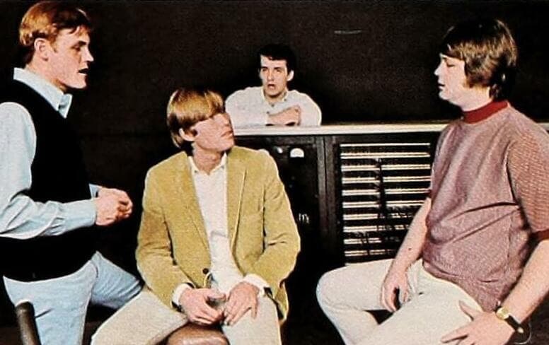 Four young men sitting and talking in a recording studio in front of a control-room window