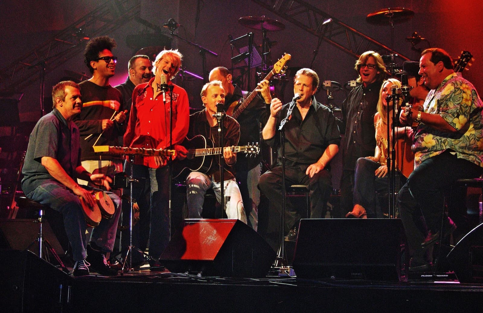 A large band on a lit stage, singers and guitarists in a row behind microphones