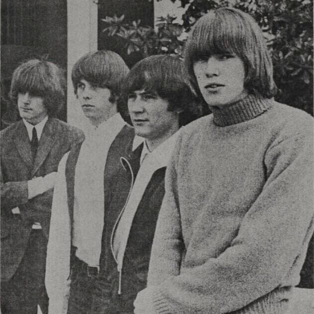 Four young men sitting together on a step in jackets, black and white