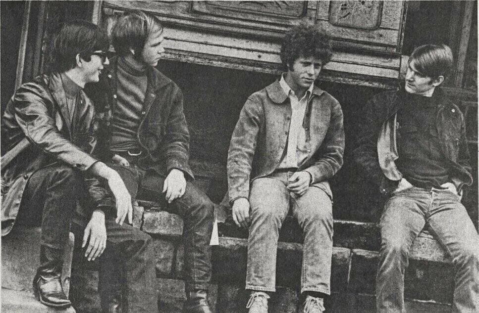 Four young men in casual clothes sitting outdoors on a stone ledge, black and white
