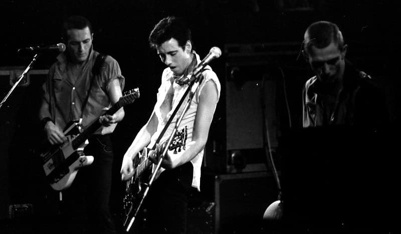 Strummer, Jones and Simonon playing side by side on a dark stage