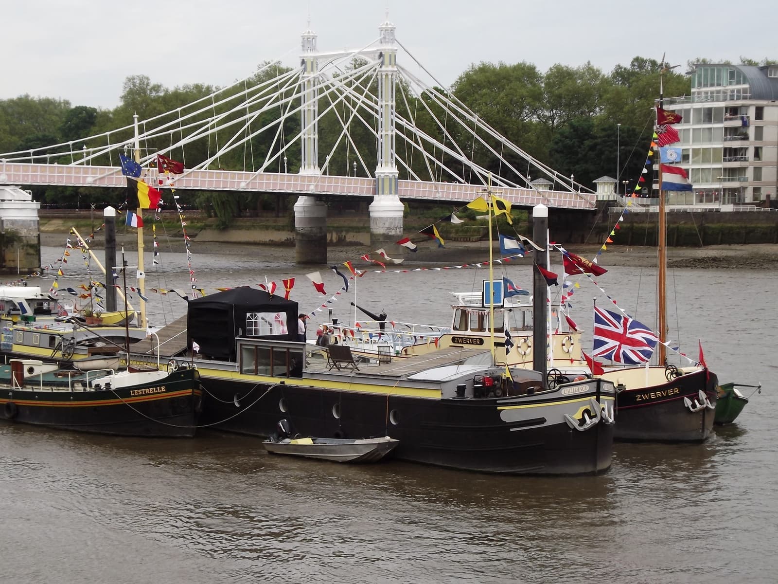 Boats moored at a pier below the white suspension cables of Albert Bridge