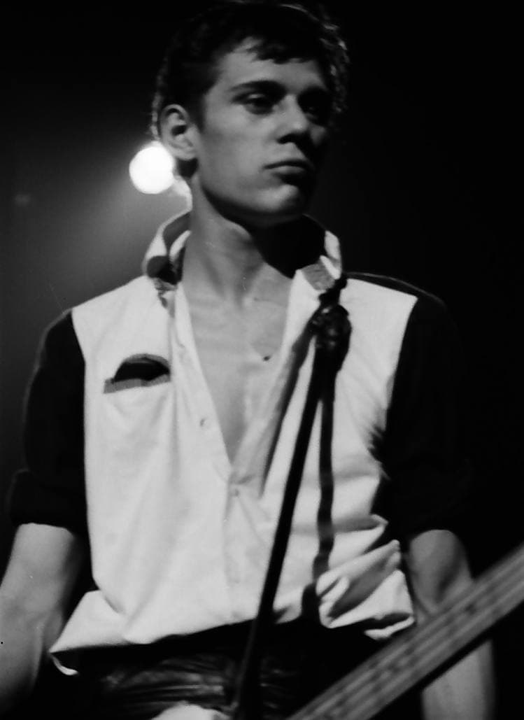 Paul Simonon at the microphone in a sleeveless two-tone shirt, black and white