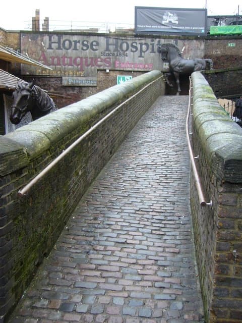 A cobbled ramp between brick walls, with a bronze horse at the top