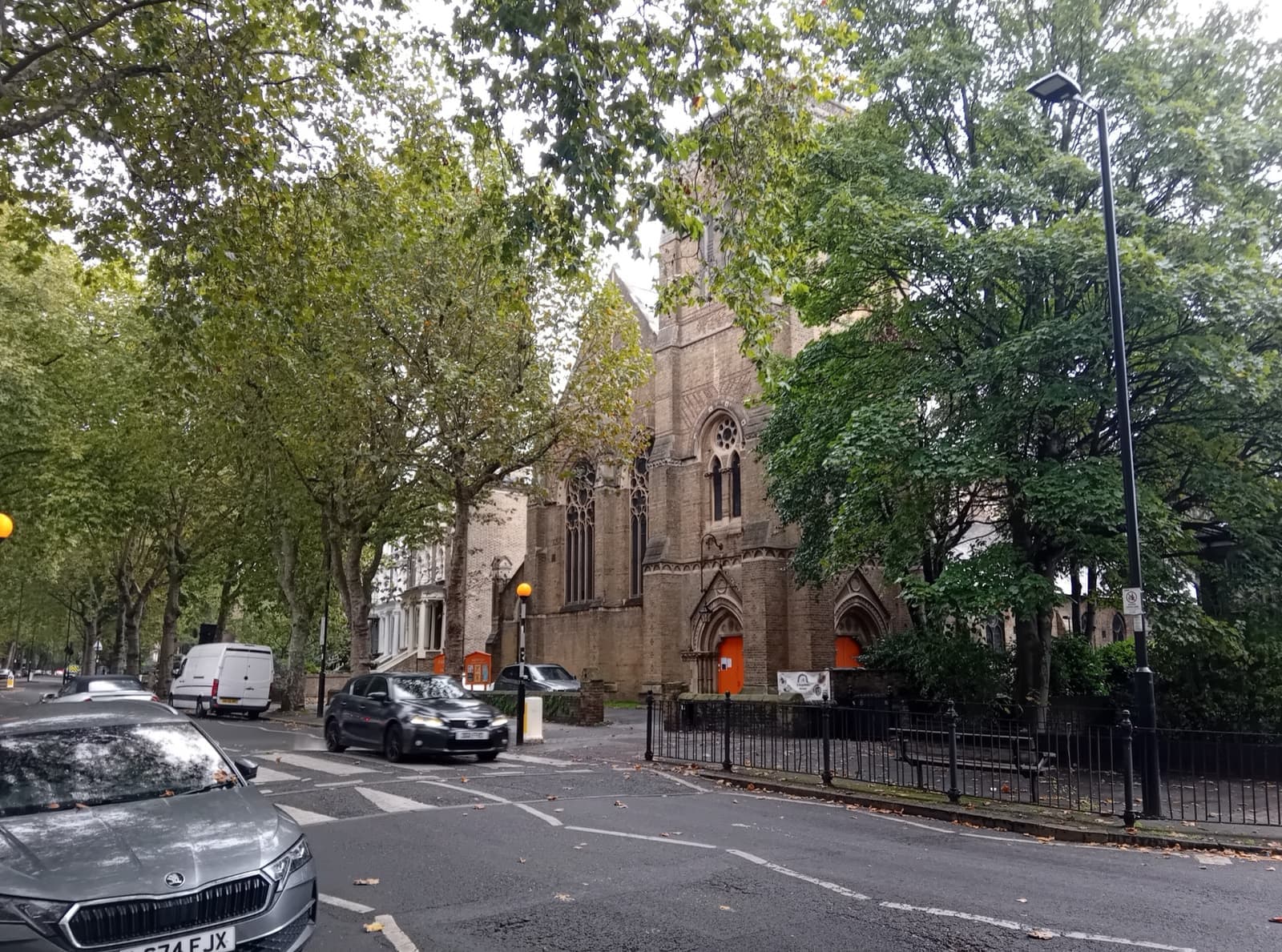 A Victorian Gothic church behind trees on a quiet street