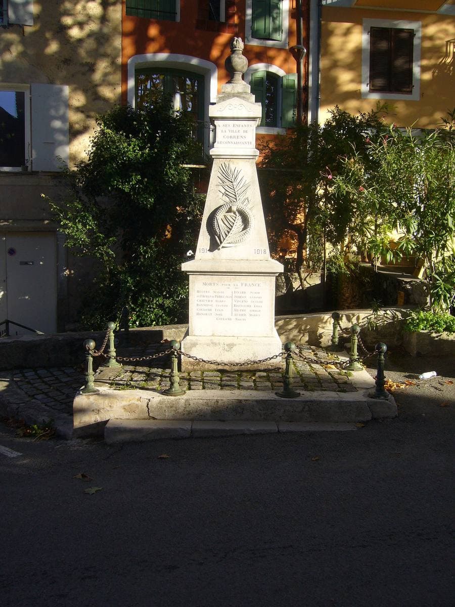 A white stone war memorial in a small Provençal square at dusk, with house fronts behind