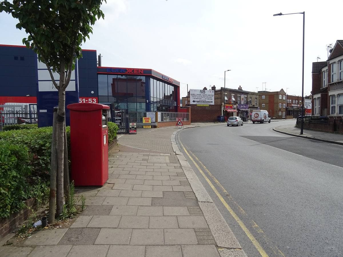 A wide suburban London high road with a red pillar box on the pavement and low shops in the distance