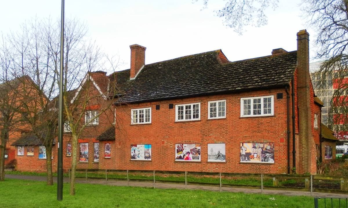 A long red-brick house with tall chimneys and white windows behind a lawn and railings