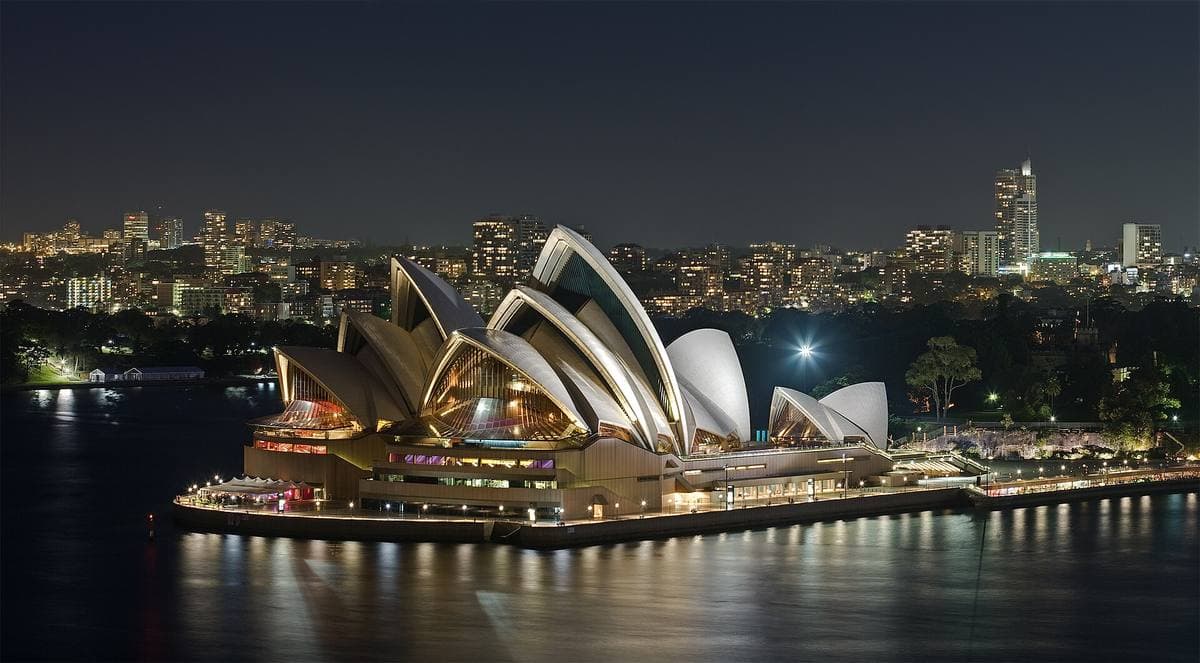 The white shells of Sydney Opera House lit at night on the harbour, the city towers behind