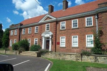 A two-storey red-brick school building with white sash windows and a pillared doorway behind a low wall