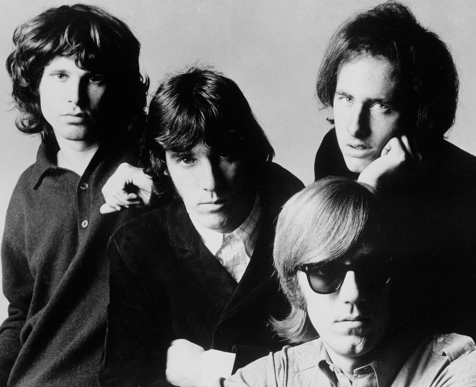 The four Doors in a black-and-white studio portrait: Jim Morrison on the left, Ray Manzarek in dark glasses at the front