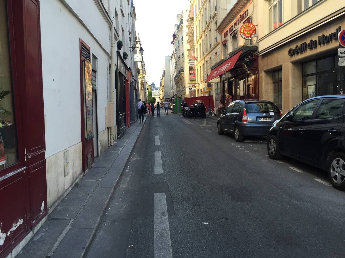 A narrow Paris street of pale stone buildings with cars parked along one side