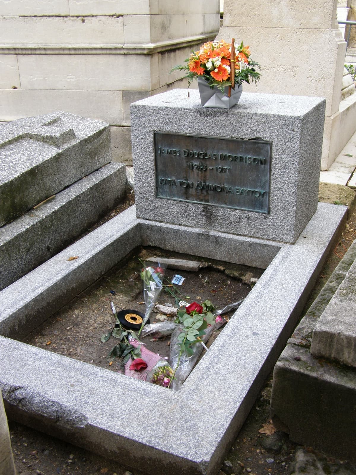 A plain stone grave with a bronze plaque, flowers laid in front