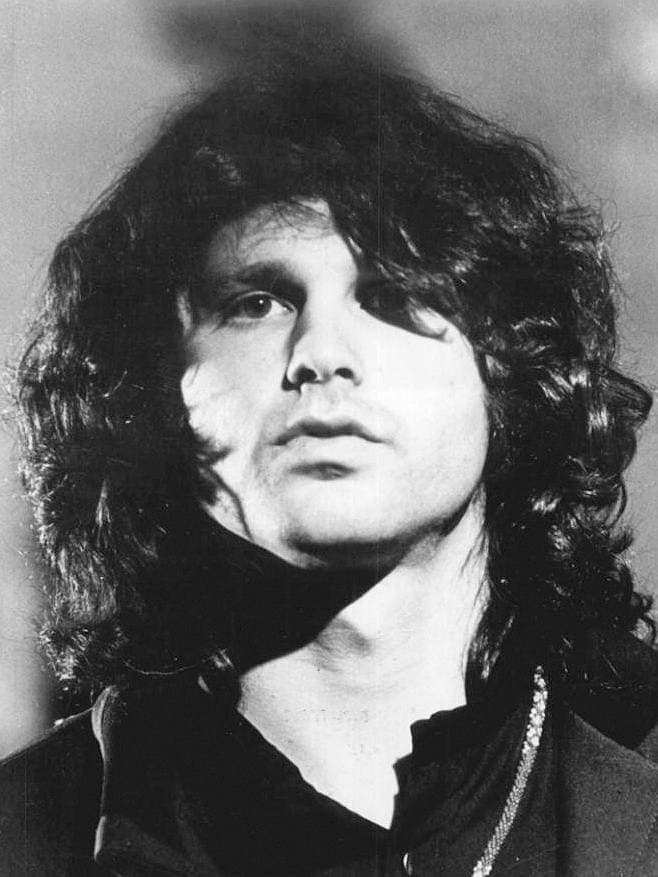 Jim Morrison in black and white, long curly hair, looking past the camera