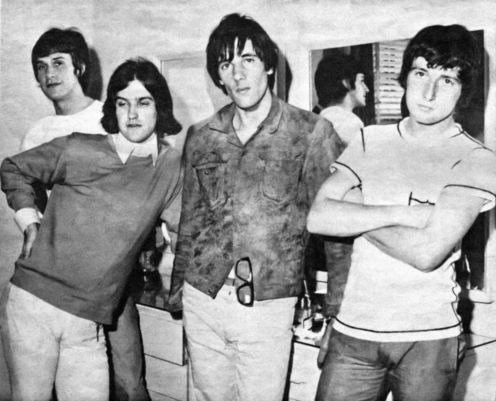 The four Kinks in 1965, in shirts and jumpers, posing in a hotel room, black and white