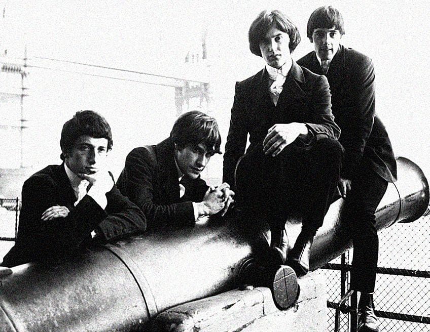 Four young men in dark suits leaning on an old cannon by the river, Tower Bridge in the background
