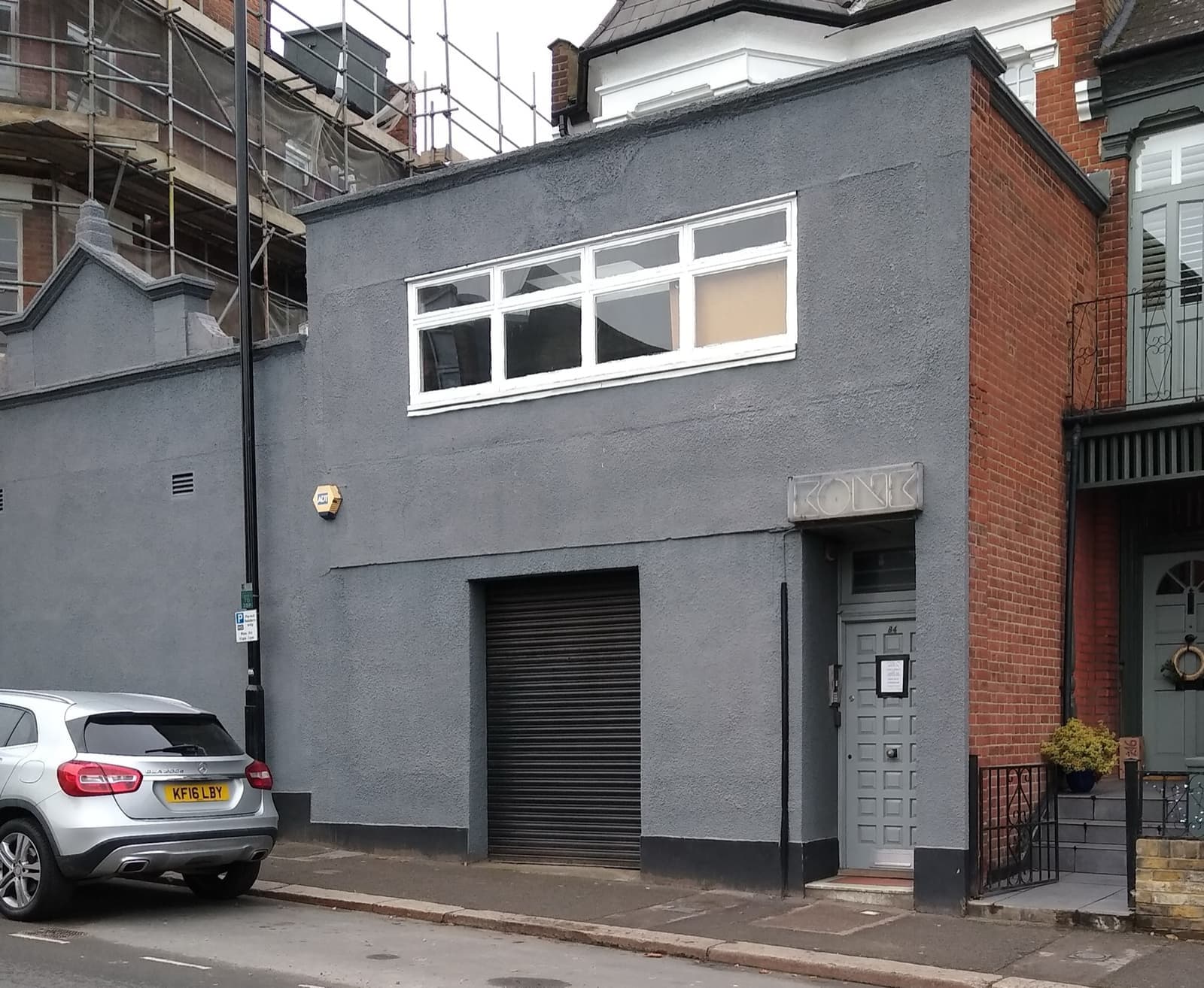 A plain grey rendered studio building with a roller door on a residential street