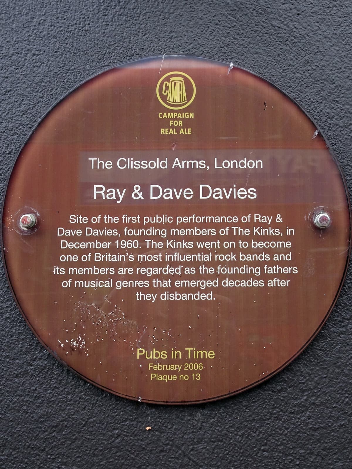 A round brown plaque on a dark wall marking the first public performance of Ray and Dave Davies